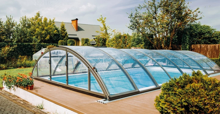 großer privater Swimmingpool in Garten mit geschlossener kuppelförmiger Plexiglasabdeckung. Sommerliches Wetter, Sträucher im Hintergrund