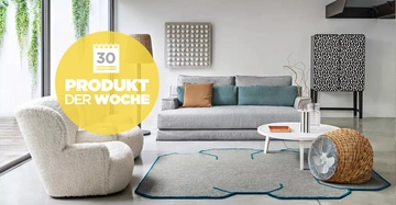 Großes cremefarbenes Schafwoll-Sessel steht neben einem grauen Sofa in einem modernen Wohnzimmer, dekoriert mit einem Teppich und einem Couchtisch. Text: 30 Produkt der Woche.