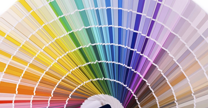 Ein Fächer mit zahlreichen Farbkarten zeigt eine Vielzahl von Farbtönen von Gelb und Grün über Blau bis Lila in einem halbkreisförmigen Muster auf einem weißen Hintergrund.