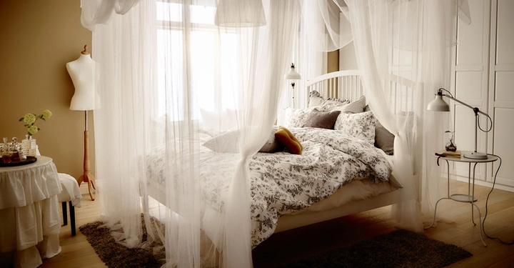 Galerie-Bild 13: Bett mit weißem Baldachin und Blumenbettwäsche Stehlampe und Schreibtischlampe im gemütlich eingerichteten Schlafzimmer mit hellen Wänden Holzfußboden Mannequin Blumen auf einem Tisch und Teppich auf dem Boden