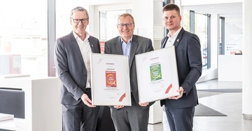 Werner Beutelmeyer überreicht zwei Urkunden an Johann Brandstetter, links von ihm stehend, und Niklas Abl, rechts von ihm stehend. Alle drei lächeln in die Kamera.