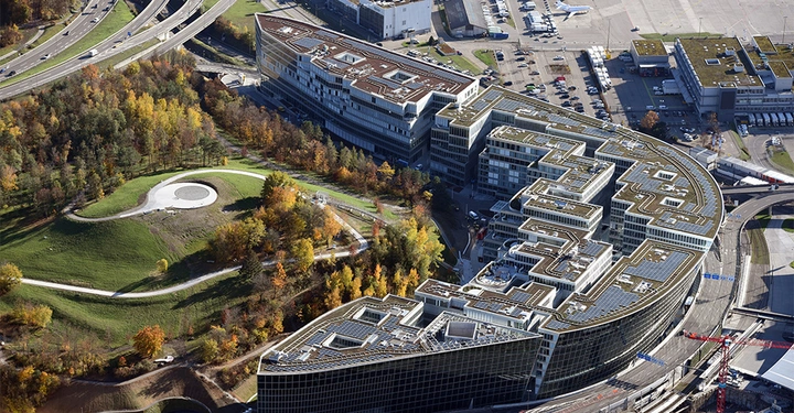 Luftaufnahme von The Circle am Flughafen Zürich. Kreisrunde Gebäudeanordnung, in der Mitte parkähnliche Anlage mit viel Grün.