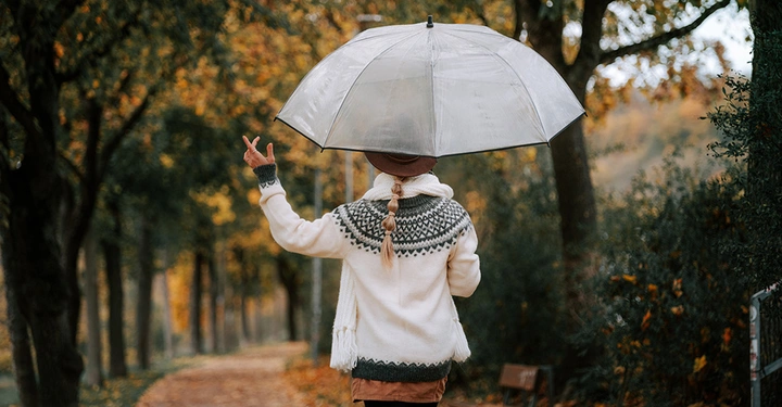 Frau mit transparentem Regenschirm beim Spaziergang an einem trüben Herbsttag, Symbolbild für Lichtmangel als Auslöser für Winterdepression.