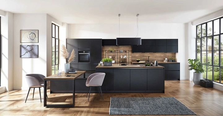 Moderne Küche mit schwarzen Schränken und Holzakzenten in einem Raum mit großen Fenstern. Ein Esstisch mit zwei Stühlen steht im Vordergrund, Pflanzen und Kunstwerke ergänzen die Dekoration.