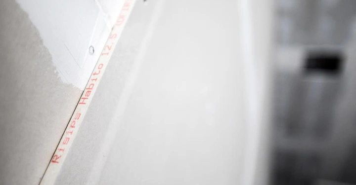 Graue Wand mit teilweise aufgetragenem weißen Putz Text auf der Wand Rigis Habito 12 5 (WU) mm unscharfer Hintergrund mit weiteren Gebäudestrukturen.