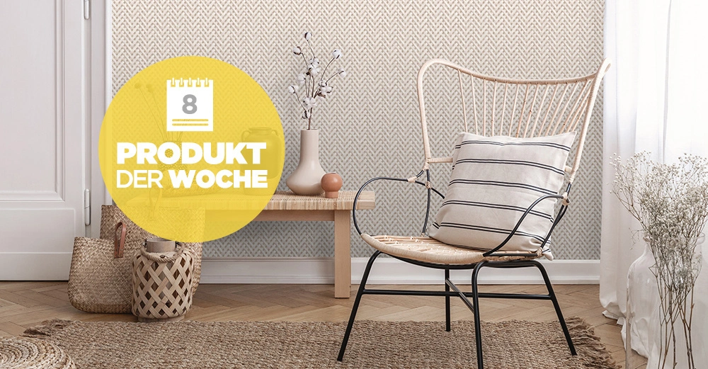 Ein Rattanstuhl mit gestreiftem Kissen steht vor einer gemusterten Wand in einem gemütlichen Raum neben einem Holztisch mit Vase und Korb. Text: "PRODUKT DER WOCHE".