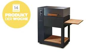 Grill mit Deckel und seitlichem Tisch in modernem Design steht vor weißem Hintergrund. Gelbes Emblem zeigt Kalender 14 und Text PRODUKT DER WOCHE.