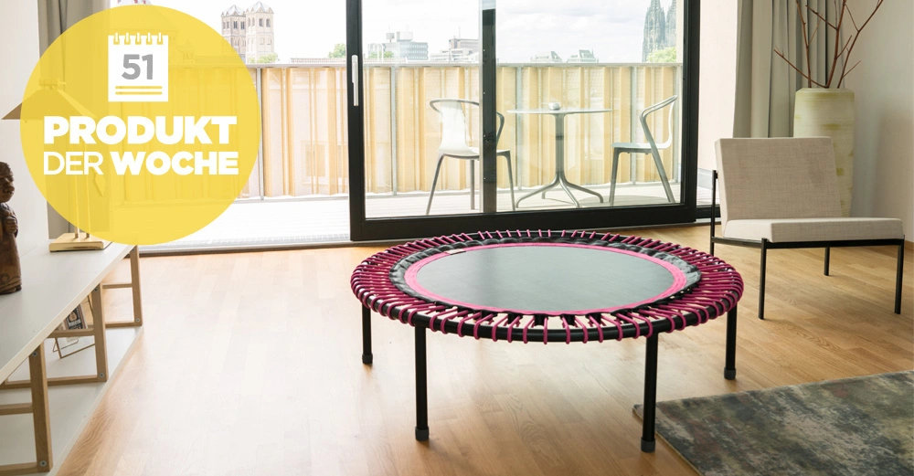Trampolin stehend im Wohnzimmer vor einer großen Fensterfront die auf einen Balkon mit Stühlen und Tisch führt. Text: 51 PRODUKT DER WOCHE.