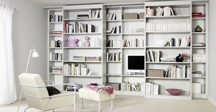 Galerie-Bild 5: Weiße Bücherregale sind mit Büchern und Dekorationsgegenständen gefüllt Ein weißer Sessel steht neben einem weißen Hocker mit Textilien Ein Stehlampe steht neben dem Sessel Der Raum ist in hellen Farben gehalten