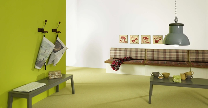 Grüne Bank mit Zeitungen daran hängend neben gelber Wand Bank davor mit Tüchern und Bank rechts mit Kissen darüber drei Bilder mit der Aufschrift SEAfood leuchtende Hängelampe darüber