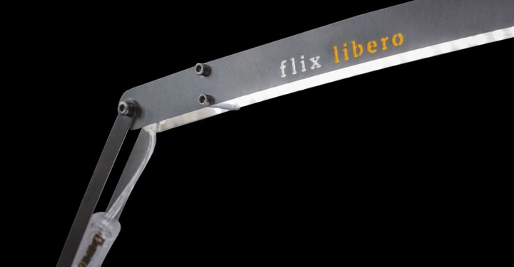 Metallischer Lampenarm leuchtet dunklen Hintergrund auf. Text flix libero auf dem Metallbügel ist sichtbar. Transparents Kabel verläuft durch den Arm.