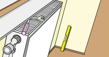 Ein weißer Heizkörper an der Wand. Ein Schraubenschlüssel und ein Schraubendreher liegen darauf. Ein gelbes Werkzeug steht an der Wand neben dem Heizkörper. Zimmer mit braunem Boden und hellem Hintergrund.