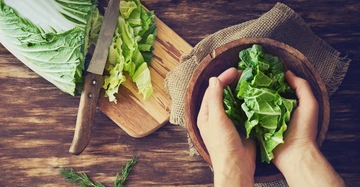 Hände halten Salatblätter über einer Holzschüssel Holzmesser und geschnittene Salatblätter auf einem Schneidebrett auf einem Holztisch Dill neben dem Schneidebrett