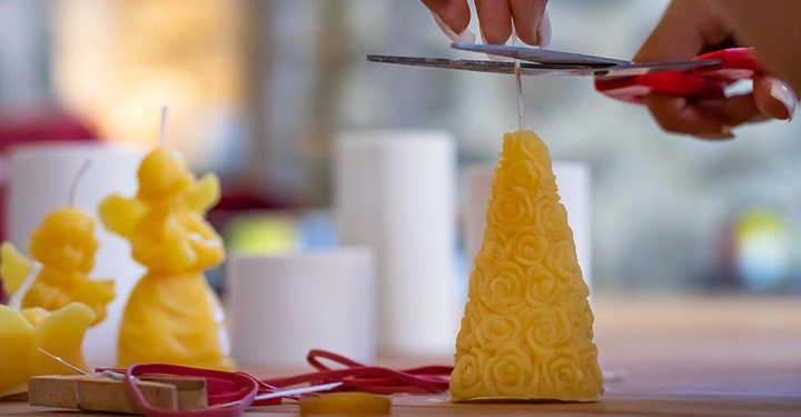 Eine Frau schneidet den Docht einer selbstgemachten Kerze aus Bienenwachs mit einer Schere zurecht.