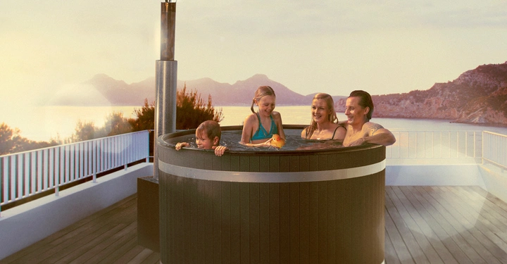 Galerie-Bild 7: Eine Familie badet in einem runden Whirlpool auf einem Balkon. Im Hintergrund sind ein See und Berge bei Sonnenuntergang zu sehen.
