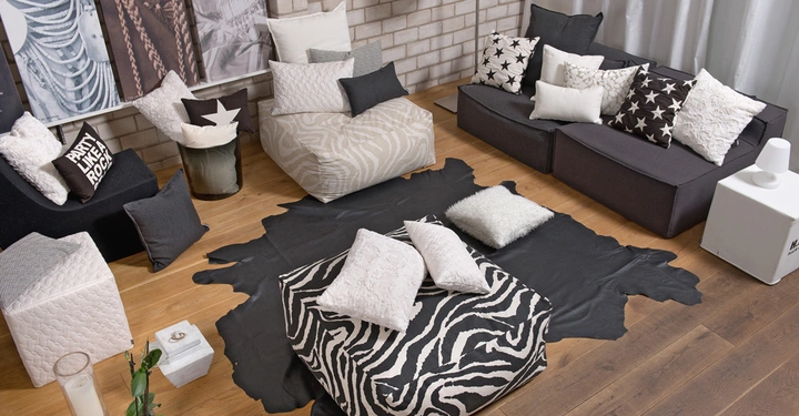 Galerie-Bild 8: Möbel mit Kissen und Decken in einem gemütlich eingerichteten Wohnzimmer umgeben von gemusterten schwarz-weißen Polstern auf Holzboden vor einer Backsteinwand und Vorhängen. Text: "PARTY LIKE A ROCK STAR".