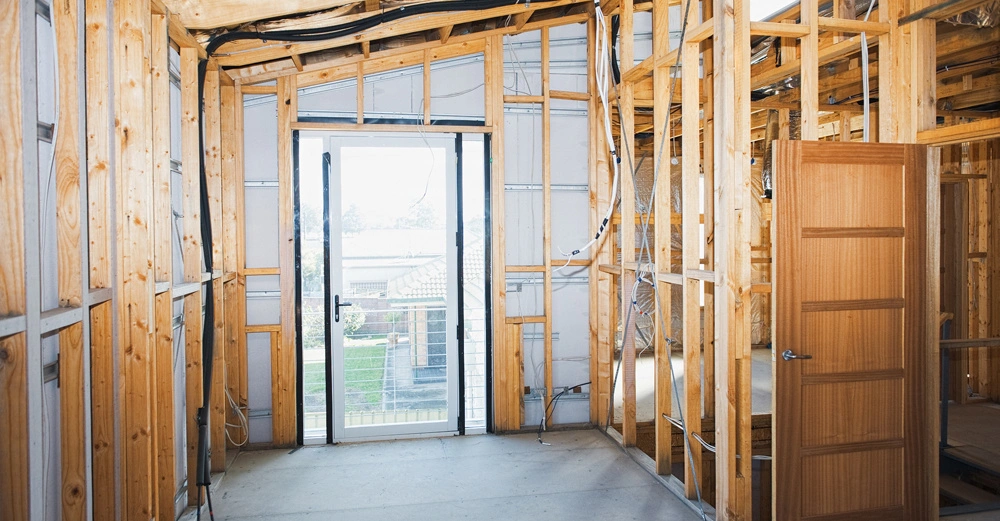 Holzrahmenstrukturen stehen in einem Raum im Bauprozess Innenansicht mit einem geöffneten Holztür und einem Glas-Schiebetür davor offener Rahmen mit sichtbaren Drähten und Isolierung im Bauumfeld