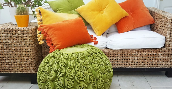 Galerie-Bild 9: Ein Rattansofa mit weißen Kissen und mehreren bunten Zierkissen sitzt neben einem Beistelltisch mit einer Topfpflanze in einem modernen Innenraum auf einem gefliesten Boden.