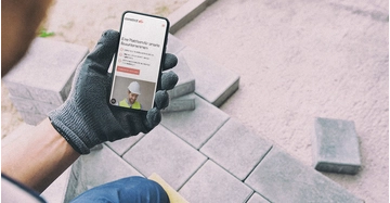 Mann mit Arbeitshandschuhen schaut auf Handy und hat dort die App constrct geöffnet.