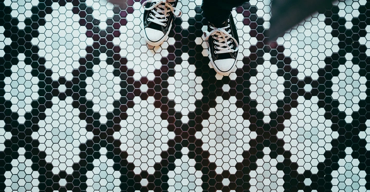 Schwarz-weiße Turnschuhe stehen auf einem weiß-schwarz gemusterten, sechseckigen Bodenfliesenmuster in Nahaufnahme.