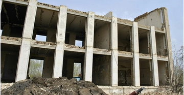 Baufälliges Gebäude mit beschädigter Fassade, freiliegenden Betonstützen und offenen Räumen auf einer Baustelle.