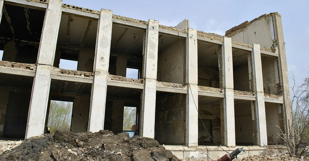 Baufälliges Gebäude mit beschädigter Fassade, freiliegenden Betonstützen und offenen Räumen auf einer Baustelle.