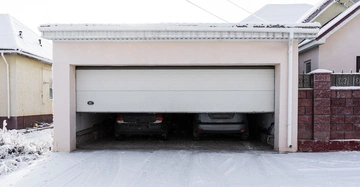 Zwei Autos stehen in einem teilweise geöffneten Garagentor in einem verschneiten Hof zwischen zwei Häusern