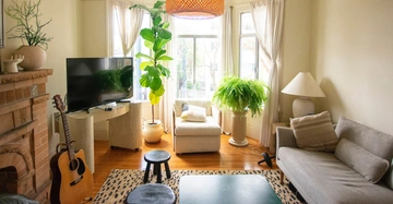 Fernseher auf kleinem Tisch neben Akustikgitarre im Wohnzimmer mit Kamin Sofa Zimmerpflanzen und großen Fenstern die Licht hereinlassen