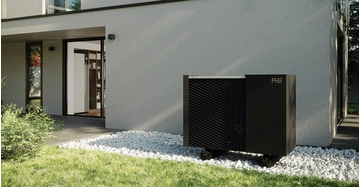 schwarze Wärmepumpe im Außenbereich auf geschottertem Grund