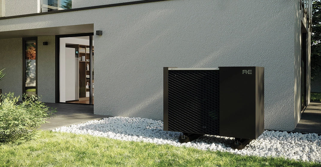 schwarze Wärmepumpe im Außenbereich auf geschottertem Grund