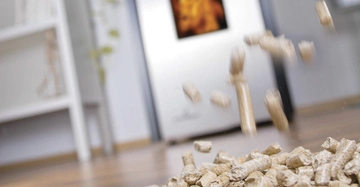 Holzpellets fallen auf einen Holzboden in einem modernen Wohnzimmer mit einem lodernden Kamin im Hintergrund und einem Bücherregal an der linken Wand