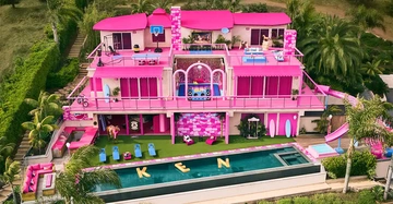 Großes mehrstöckiges Barbiehaus in Pink mit mehreren Balkonen und einer Dachterrasse umgeben von Palmen Schwimmbad im Vordergrund mit "KEN" in gelben Buchstaben auf dem Wasser