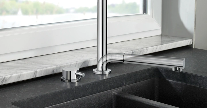 Ein silberner Wasserhahn steht über einer schwarzen Doppelspüle; im Hintergrund gibt es eine Fensterbank mit einer Marmoroberfläche und Ausblick auf eine Landschaft.