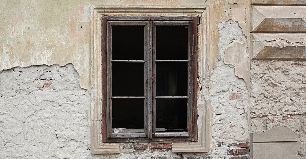 dunkelbraunes Holzfenster in alter hellbeiger und grauer Hausfassade, schöner Stuck, Fassade blättert aber schon ab, darunter Stein sichtbar, altes verlassenes Haus