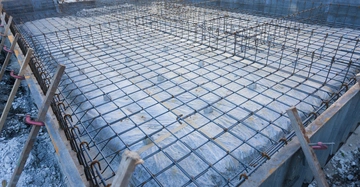 Eine Betonfundamentstruktur verstärkt durch ein Gitter aus Stahlarmierung Stäben befindet sich in einem Baustellenumfeld mit Betonplatten Unterstützung und Erdarbeiten im Hintergrund.