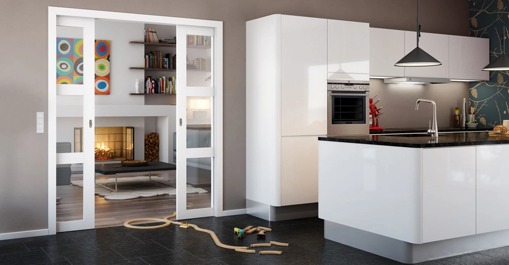 Spielzeug auf dem Boden neben einer modernen Küche mit weißen Schränken und schwarzen Arbeitsflächen angrenzend an ein Wohnzimmer mit Kamin Bücherregalen und bunter Kunst an der Wand.