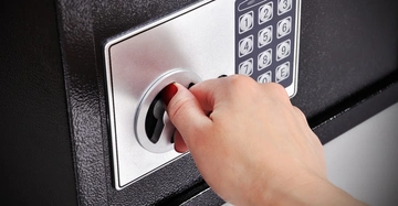 Hand dreht den Schlüssel in einem Safe mit Tastenfeld und zahlen 1 2 3 4 5 6 7 8 9 0 E im Hintergrund