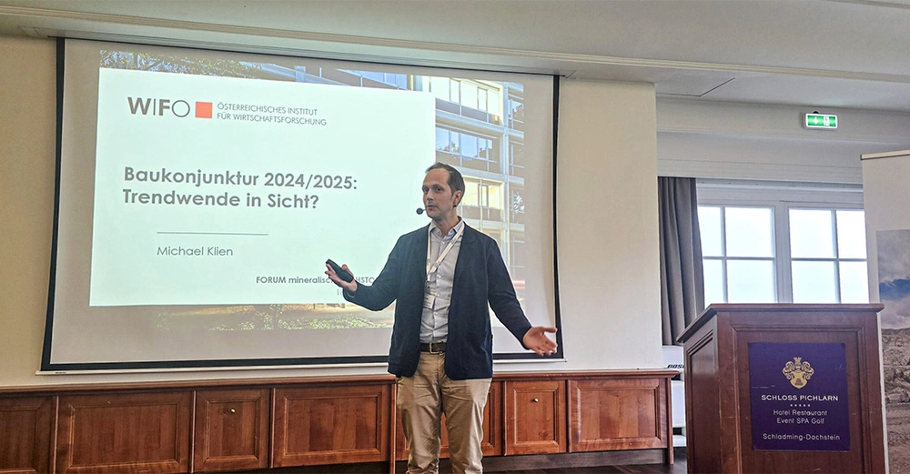 Michael Klien vom Wifo steht vor einer Beamer-Leinwand, darauf zu lesen der Titel seines Vortrags "Baukonjunktur 24/25: Trendwende in Sicht?"