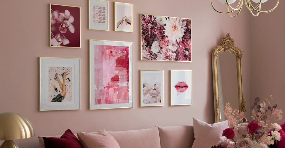 Gerahmte Kunstwerke hängen an einer rosafarbenen Wand eines Wohnzimmers, darunter Bilder von Blumen, Händen und Lippen. Oben links steht der Text JE T'AIME dreimal in goldenen Rahmen. Ein goldener Spiegel steht an der Wand; rosa Kissen und Blumenarrangement auf dem Sofa.
