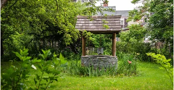 Traditioneller Schachtbrunnen mit Schindeldach in grünem Garten