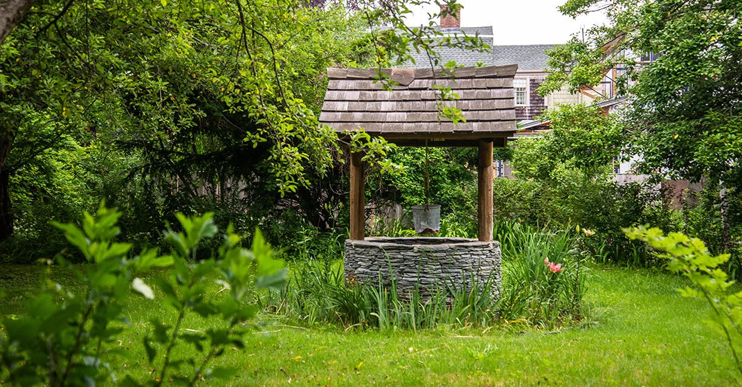 Traditioneller Schachtbrunnen mit Schindeldach in grünem Garten