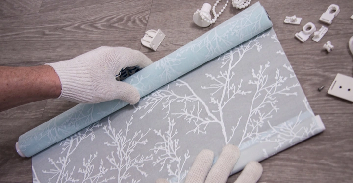 transparentes, hellblaues Innenrollo wird von jemandem mit weißen Arbeitshandschuhen montiert. Alle wichtigen Montagegegenstände liegen daneben. Vogelperspektive