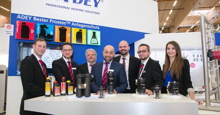 Galerie-Bild 10: Sieben Personen posieren lächelnd hinter einem Ausstellungstresen mit verschiedenen Produkten in den Händen Messehalle ADEY Professional Heating Solutions ADEY Bester Prozess™ Anlagenschutz Halle 21 D810