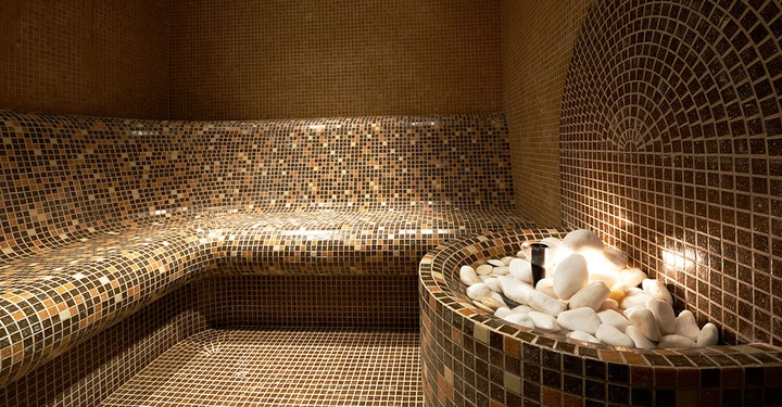 Türkisches Dampfbad in dunklen Farben mit Sitzbank um die Ecke und einem Becken mit Handtuchablage im Vordergrund.