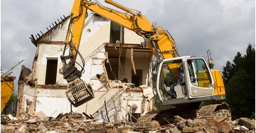 Altbau in Wohnsiedlung wird von großem gelbem Bagger abgerissen