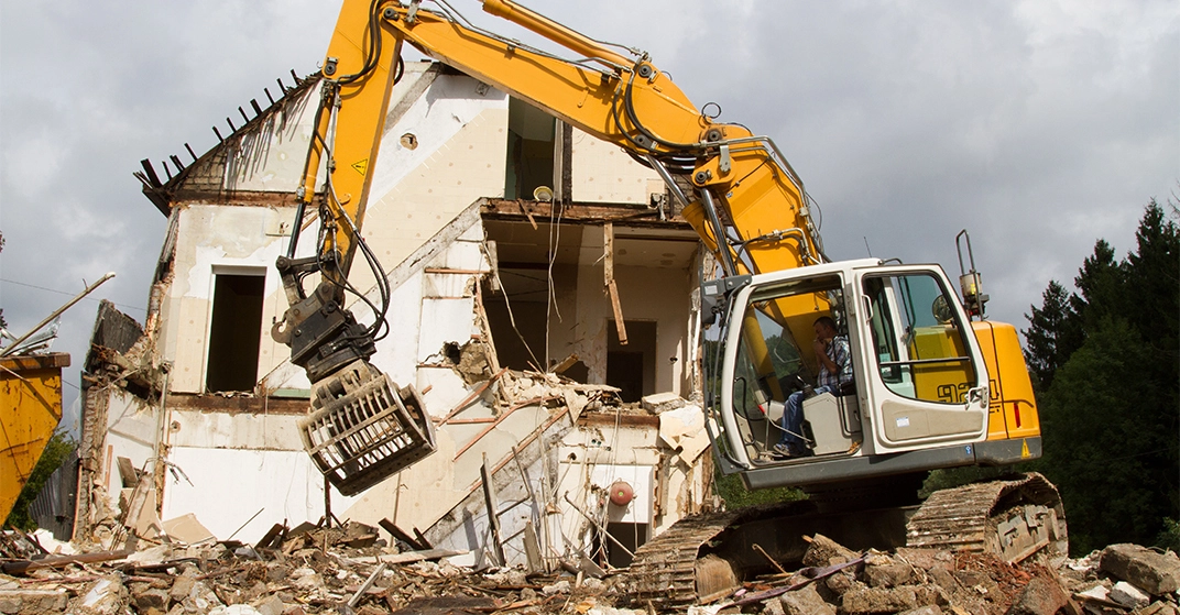 Altbau in Wohnsiedlung wird von großem gelbem Bagger abgerissen