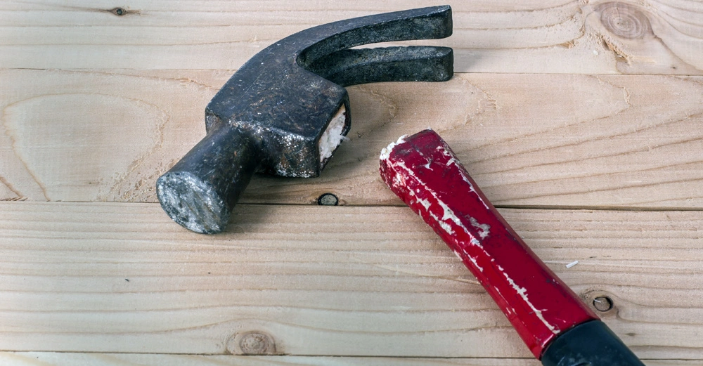 Ein Hammer mit abgebrochenem roten Griff liegt still auf hölzernem Hintergrund