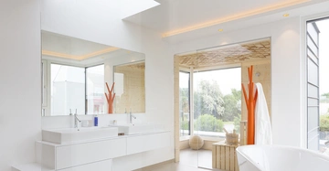 Rechteckiger Spiegel und zwei Waschbecken auf weißem Waschtisch reflektieren helle moderne Badezimmerumgebung mit Glaswand Innensauna draußen mit Bäumen und grüner Landschaft.