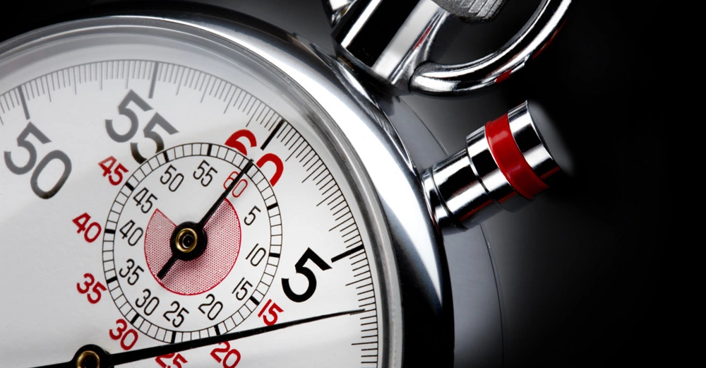 Stoppuhr, die gestoppt wird, in einer Nahaufnahme auf schwarzem Hintergrund. Zifferblatt zeigt Sekundenmarkierungen, großer roter Zeiger bei 60 Sekunden, kleinerer Zähler innerhalb des Zifferblatts