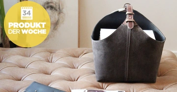 Ledertasche sitzt auf einem gepolsterten Ledersofa enthält Papiere und eine nahegelegene Mappe sowie Zeitschriften ein gelber Kreis enthält die Texte 34 PRODUKT DER WOCHE in moderner Wohnung.